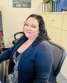 A woman sitting in an office chair wearing a blue jacket.